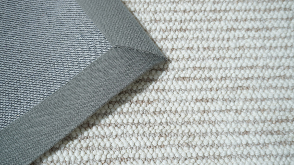 Close-up of the Vesper rug's corner, its grey binding folded back over the ivory loops.