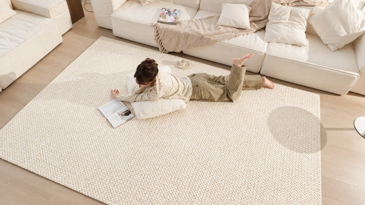 A person lying on Dapple rug, reading beside a white sofa in soft daylight.