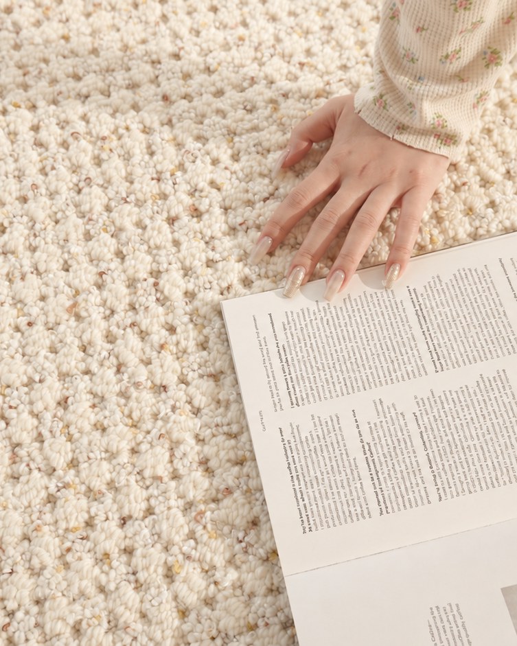Close-up of a hand resting on Dapple's cream loop texture beside an open newspaper.