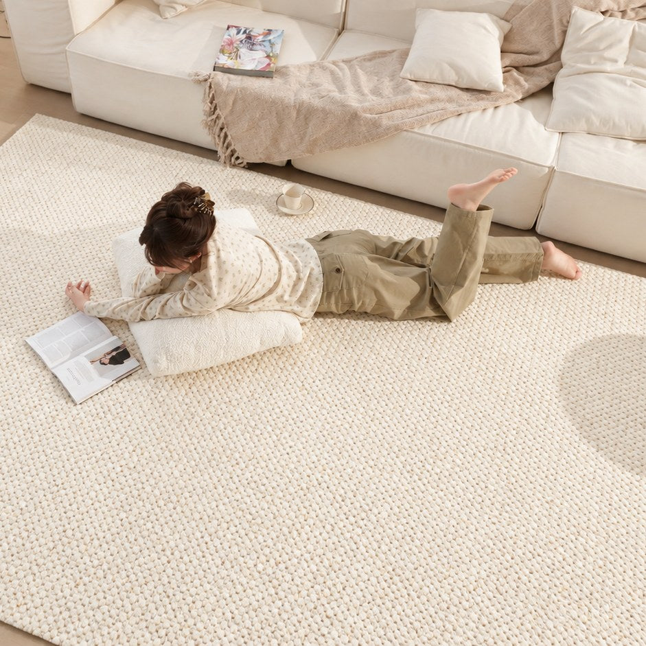 A person lying on Dapple rug, reading beside a white sofa in soft daylight.