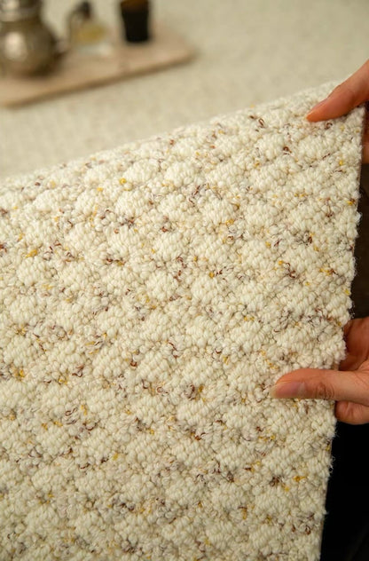 Dapple rug held up by hand, showing its flecked cream loop texture.