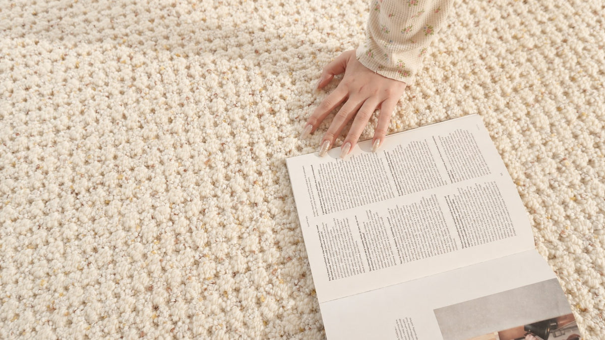 Hand on the Dapple rug beside an open magazine, showing its flecked loops.