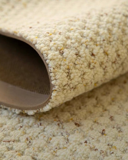 Dapple rug rolled back to show its brown backing and flecked cream pile.