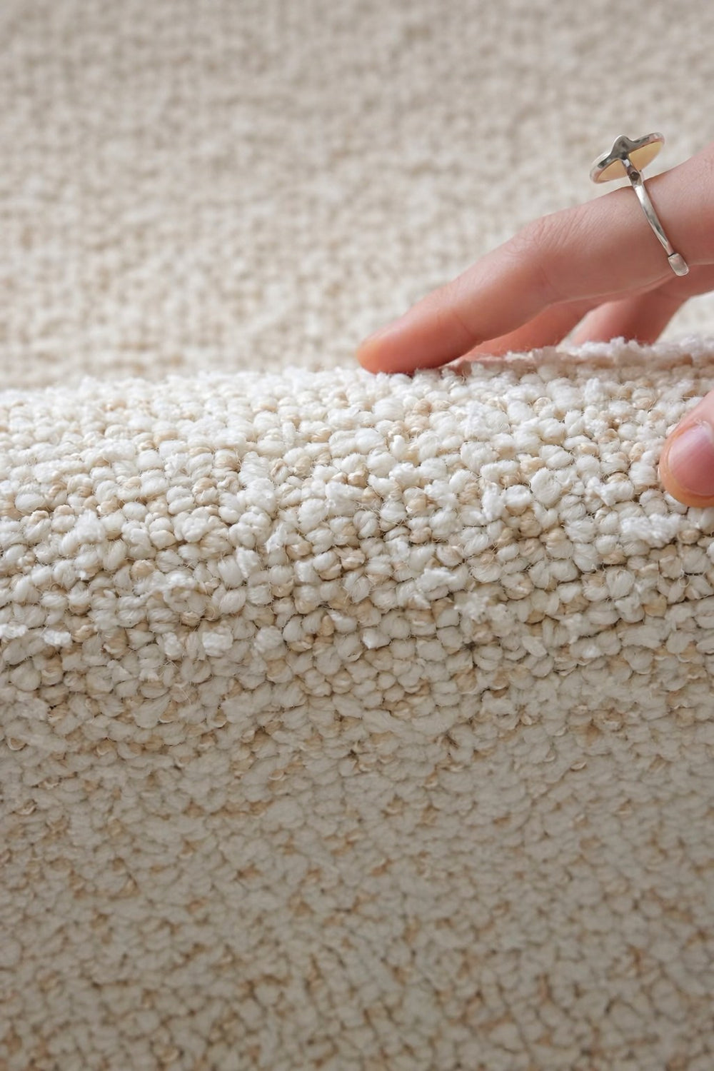 Hand lifting the edge of the Daybreak rug, showing its soft ivory bouclé pile.