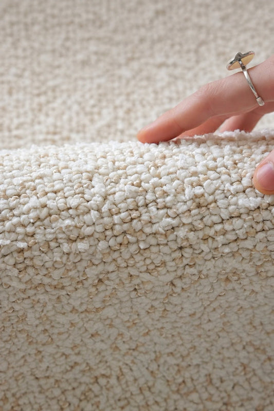 Hand lifting the edge of the Daybreak rug, showing its soft ivory bouclé pile.