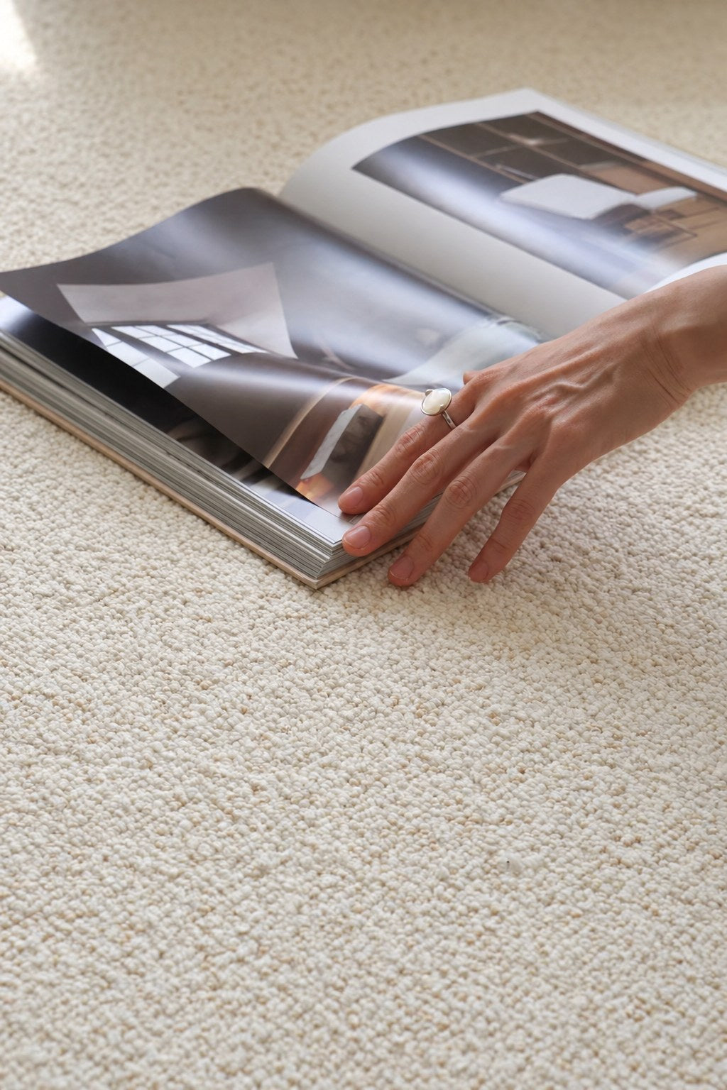 Hand on an open magazine resting on the Daybreak rug's ivory bouclé.