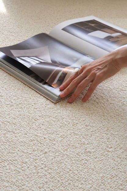 Hand on an open magazine resting on the Daybreak rug's ivory bouclé.