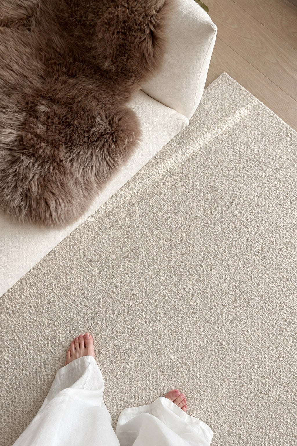 Looking down at bare feet on the Daybreak rug beside a white sofa and a sheepskin.