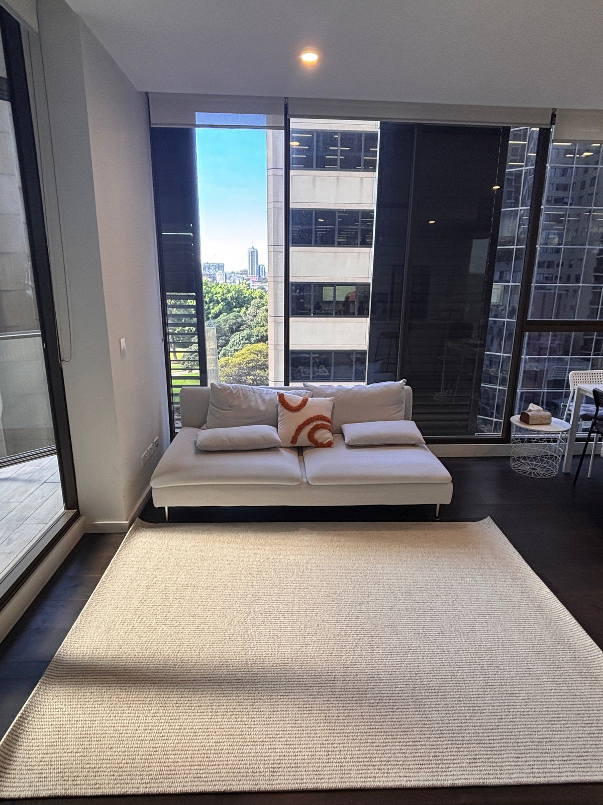 Glint rug in a high-rise living room in front of a white sofa, with city views through floor-to-ceiling windows.
