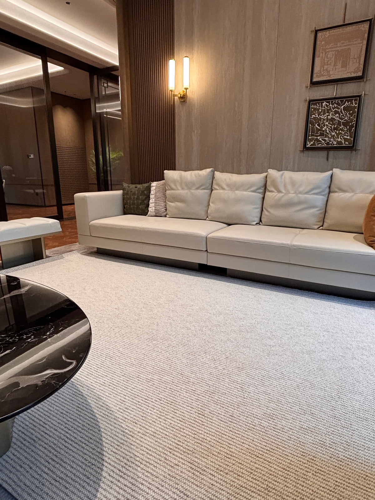 Glint rug under a marble coffee table in a lounge with a long cream sofa and timber-panelled walls.