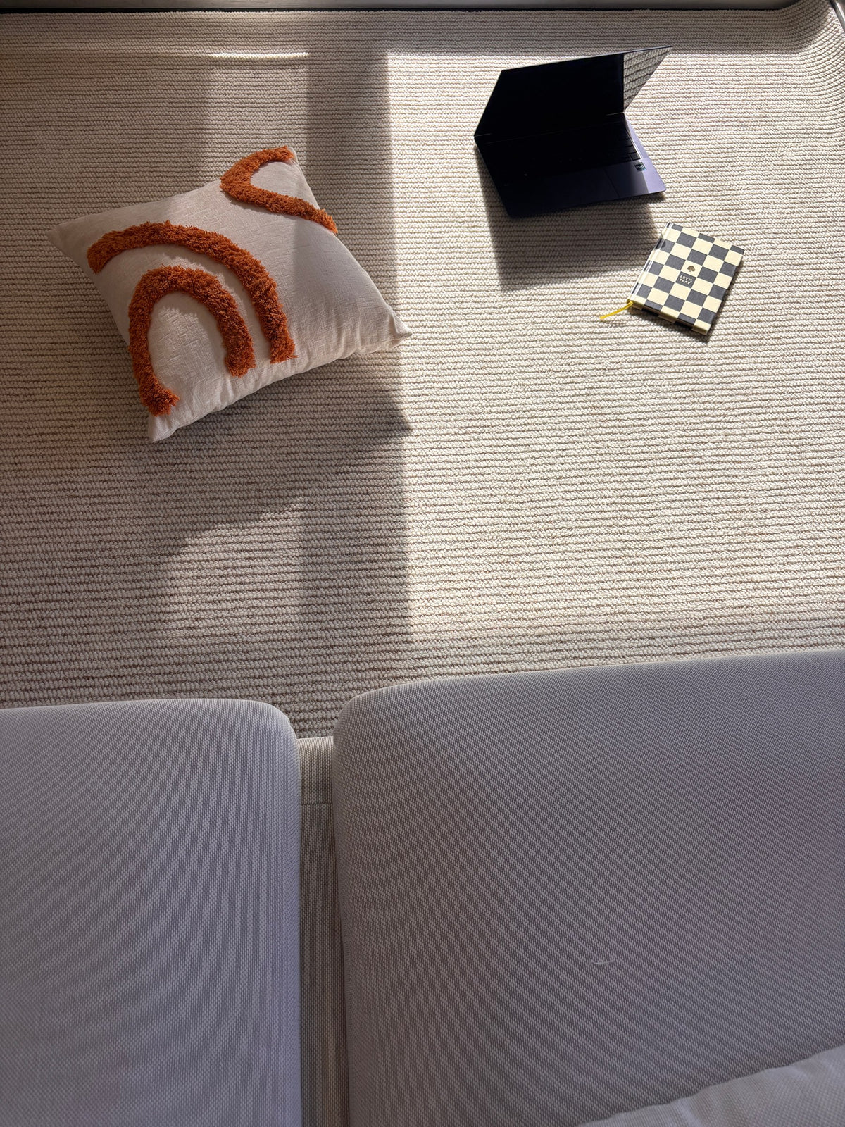 Looking down on the Glint rug between two sofas, with a cushion, a laptop and a notebook in the afternoon sun.