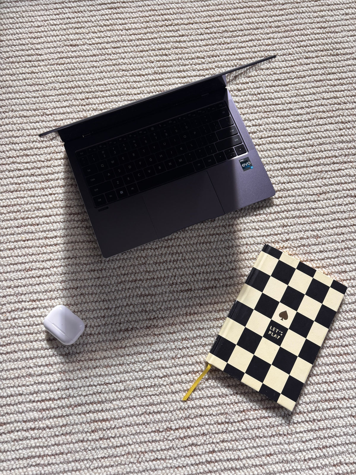 Laptop, notebook and earbuds case resting on the ribbed Glint rug.