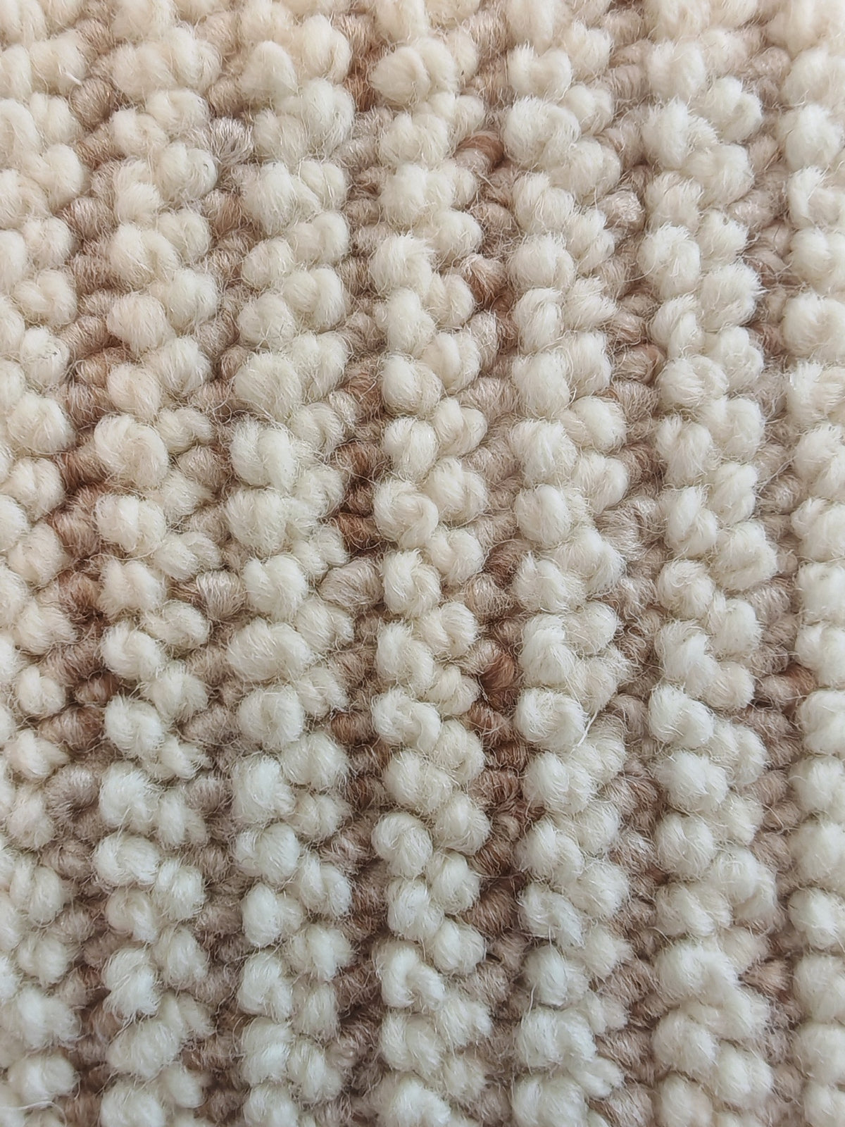 Close-up of the Glint rug's ivory loops, their fibres catching the light between soft-gold rows.
