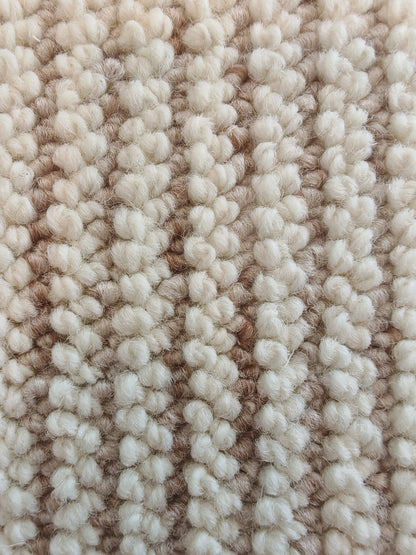 Close-up of the Glint rug's ivory loops, their fibres catching the light between soft-gold rows.