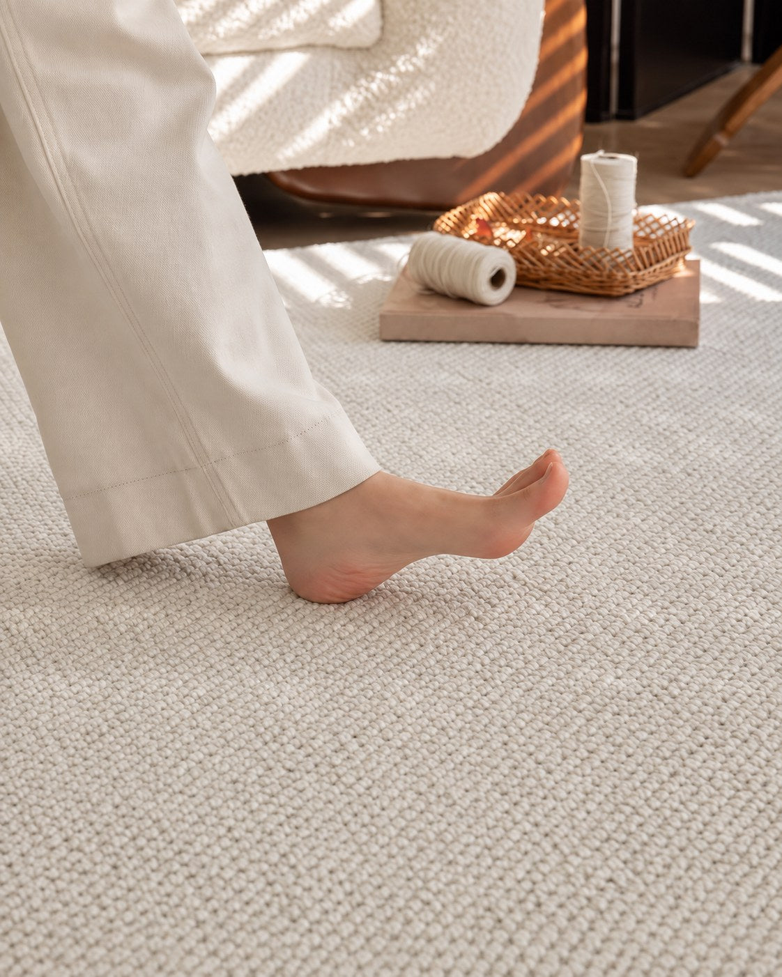 A bare foot stepping onto Halcyon's pebbled cream surface beside a tray of yarn.