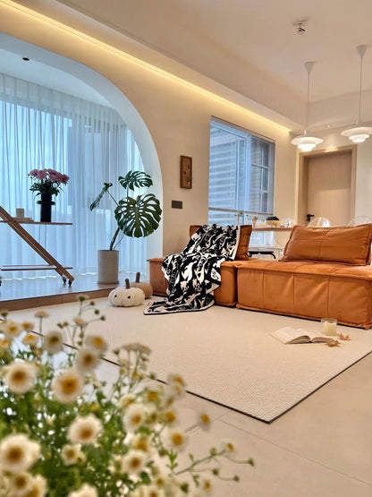 Halcyon rug in an open living room with an orange leather sofa and daisies in the foreground.