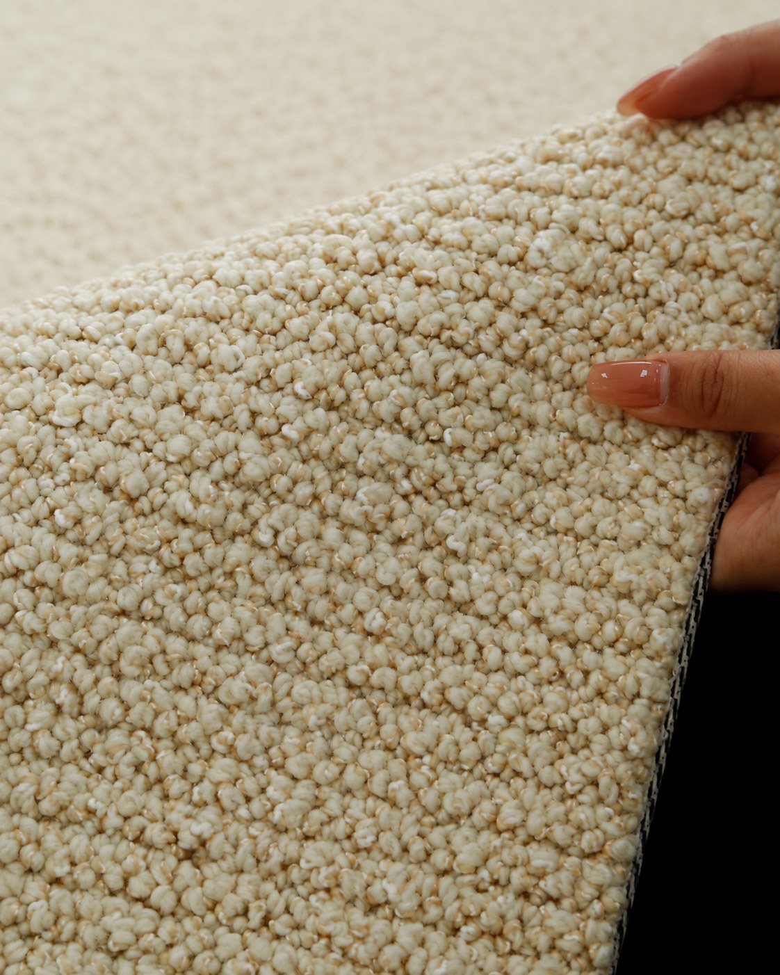 Hands lifting the edge of the Sunlit rug, showing its golden-beige bouclé loops.