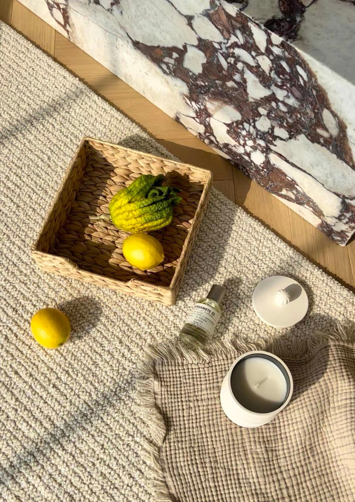 Woven basket of lemons, a candle and a linen cloth on the Sunlit rug in sunlight.
