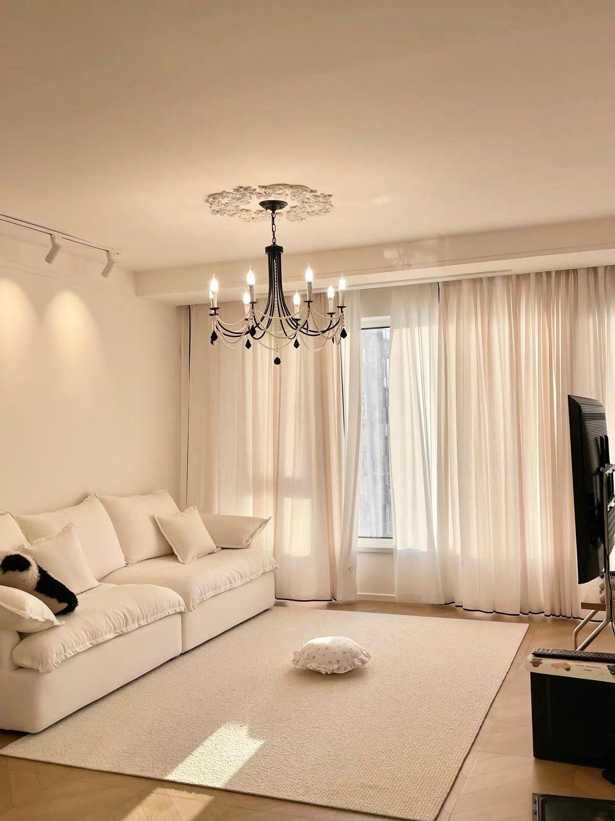 Sunlit rug in a cream living room with a white sofa and a black chandelier.
