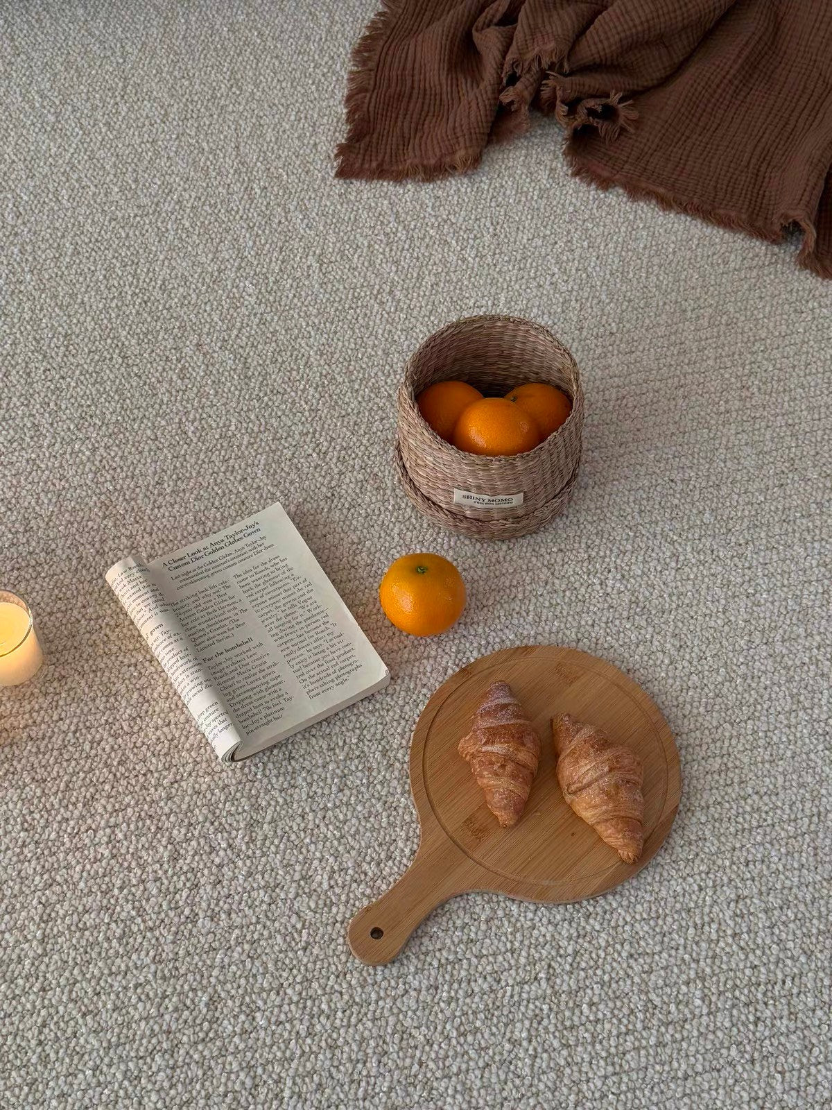 Looking down on the Sunlit rug with a book, croissants, oranges and a candle.