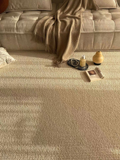 Sunlit rug in front of a beige sofa with a knitted throw and afternoon light.