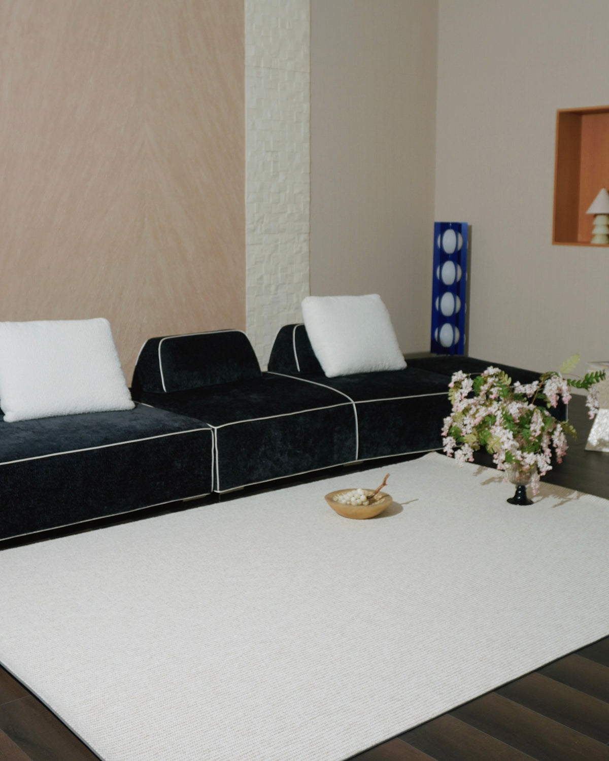 Vesper rug in a living room with a black velvet sofa, white cushions and a vase of blossom.