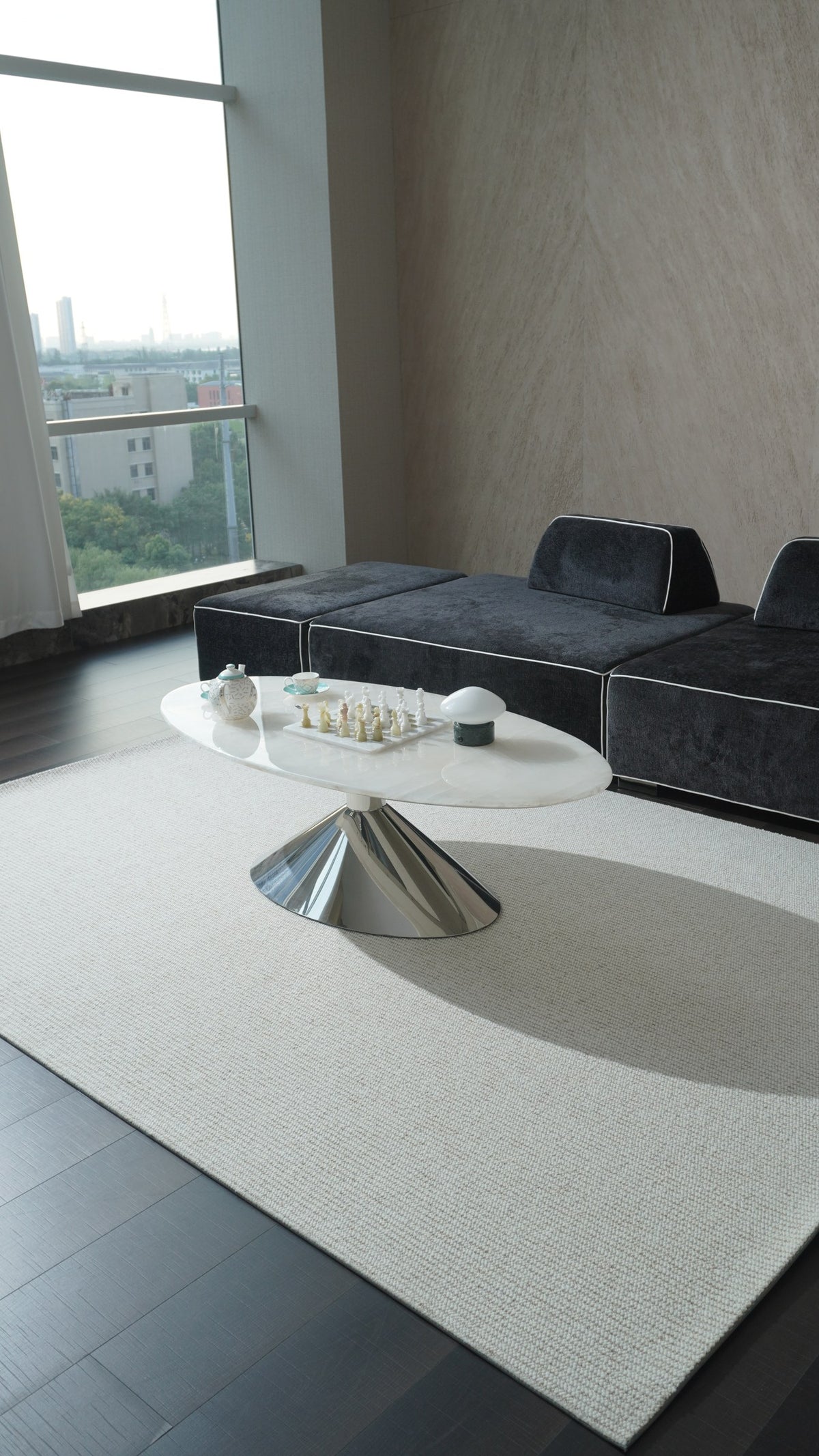 Vesper rug under an oval marble coffee table, beside a black sofa and a tall window.